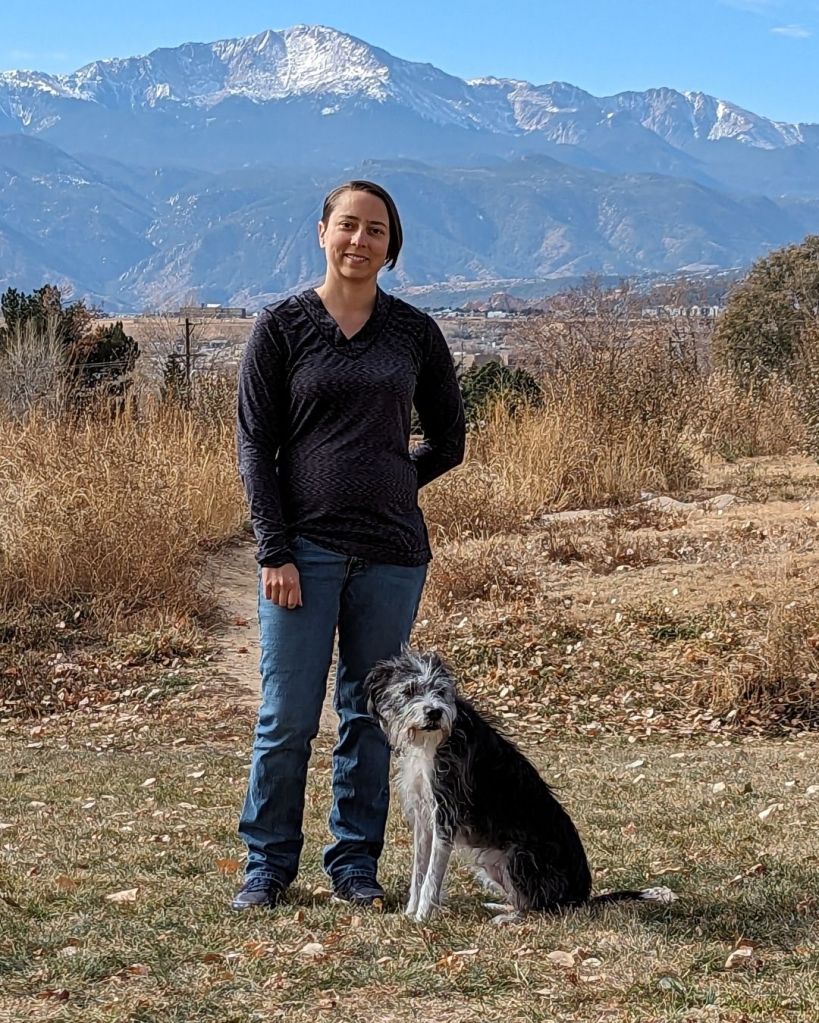 Liz Fisher, trainer, with black and white dog and mountains in the background